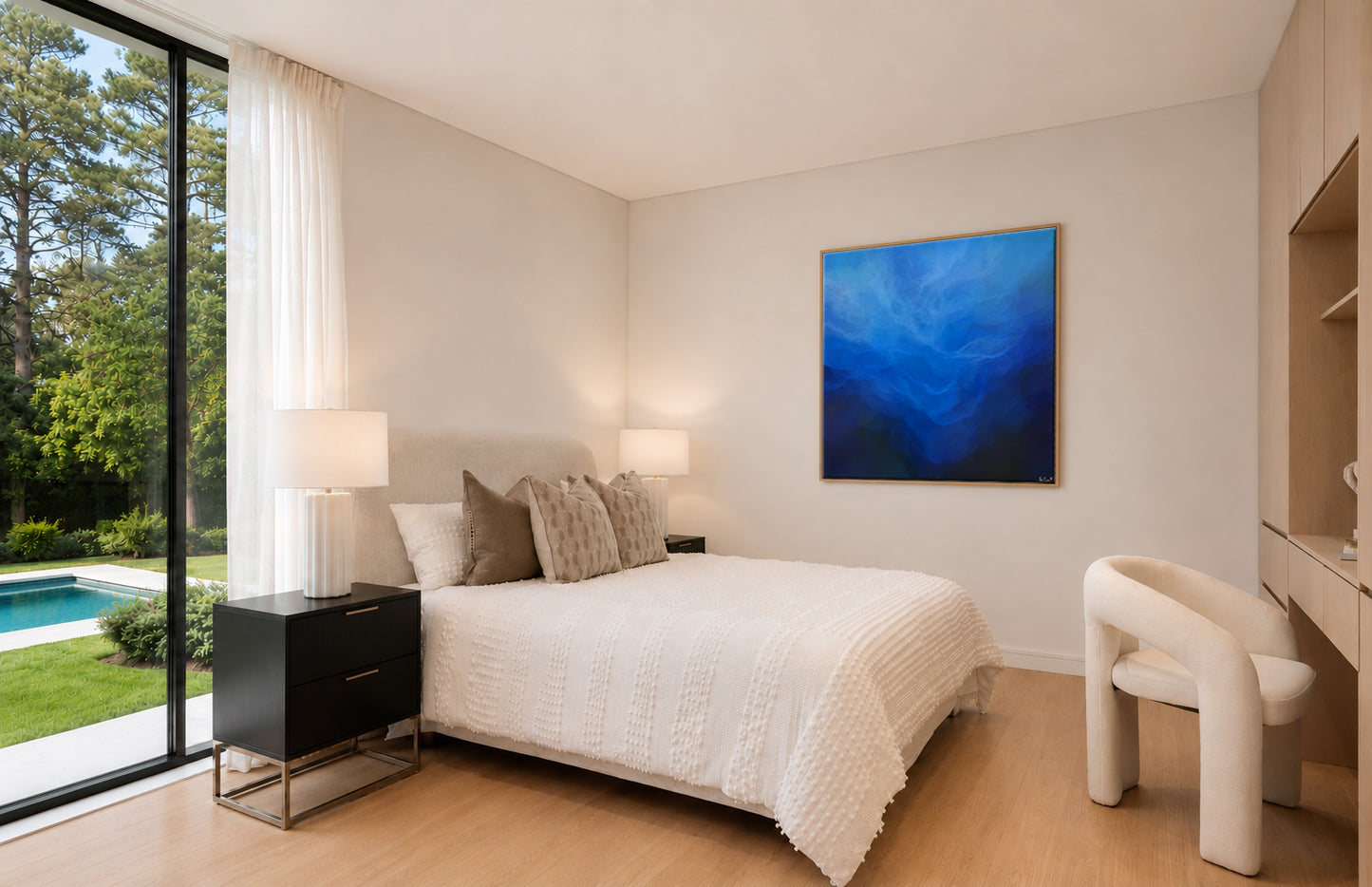 A modern bedroom interior with a bed dressed in white textured bedding, neutral pillows, a black nightstand, a white chair, and a large blue abstract wall painting. A large window on the left shows a pool and green lawn outside.